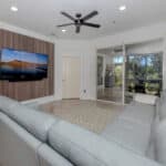 Spacious living room featuring a large flat-screen TV, white leather sofas, and natural light from g.