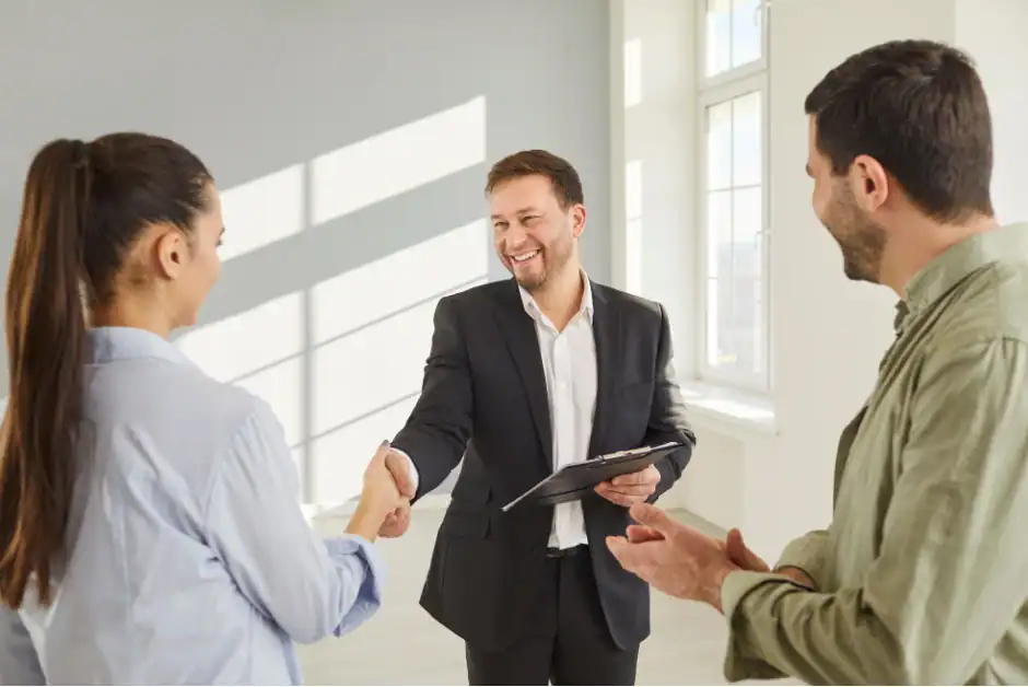 Real estate agent shaking hands with clients during consultation.